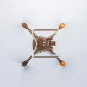 Top-down view of a white quadcopter drone with a high-definition camera mounted on its central body. Four arms extend outward, each ending with an orange warning light, showcasing a clean and modern design.