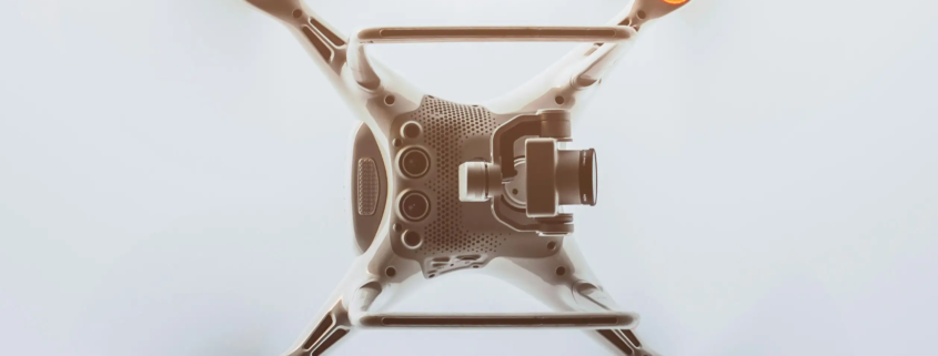 白色四旋翼無人機的俯視圖，機身中央安裝了高畫質攝影機。四條手臂向外延伸，每條手臂的末端都有一個橙色警示燈，展現出簡潔時尚的設計。.