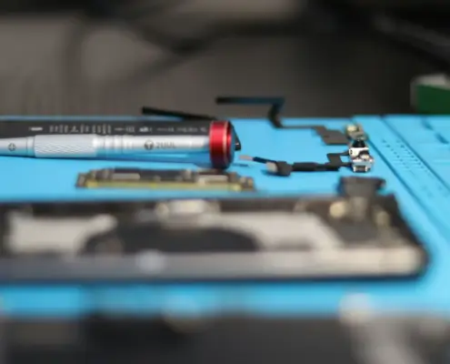 An electronics repair workbench with a blue anti-static mat. On the mat are a screwdriver, a mobile phone