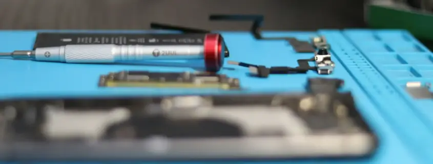 An electronics repair workbench with a blue anti-static mat. On the mat are a screwdriver, a mobile phone